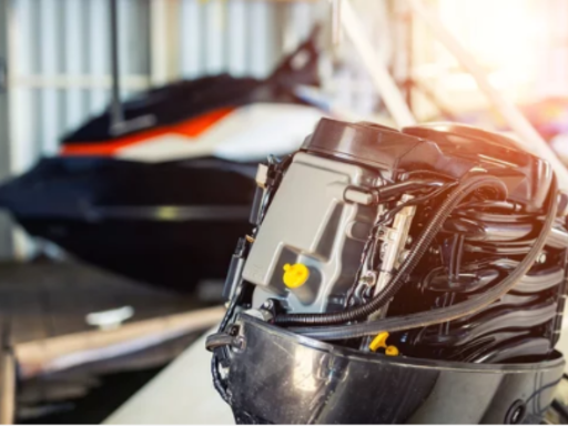 Close-up of an outboard boat engine in a workshop with a blurred jet ski in the background.